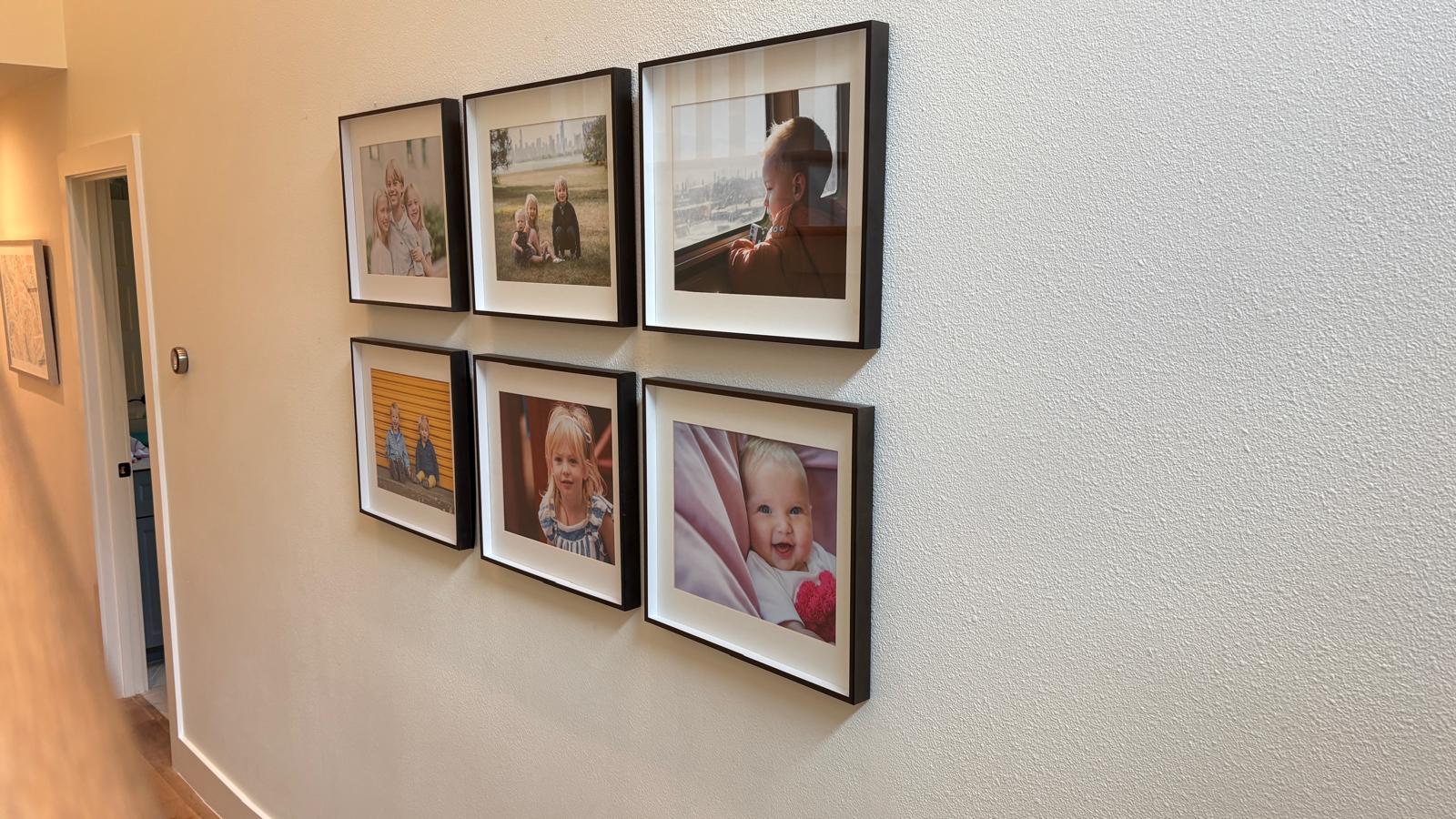 Six black-framed family photographs arranged in a grid along a hallway wall