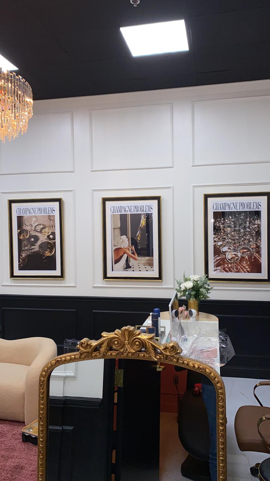 Close view of three framed champagne-themed prints on a salon wall beside a gold mirror