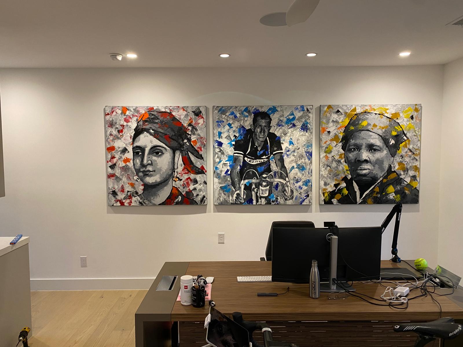 Three large painted portrait canvases mounted above an executive office desk